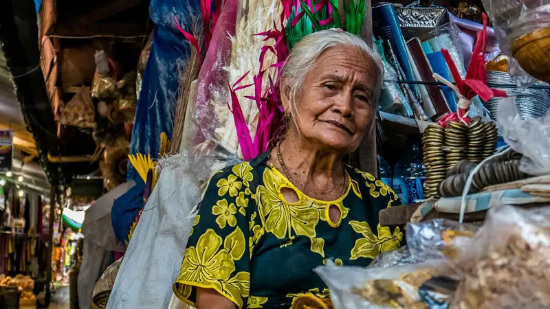 Seorang pedagang lokal di Pasar Seni Sukawati di Gianyar, Bali, dikelilingi barang-barang tradisional berwarna-warni.