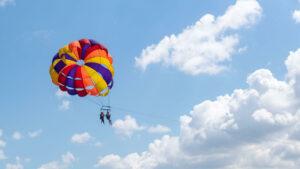 Dua orang berparasailing dengan parasut warna-warni di atas langit Bali yang cerah