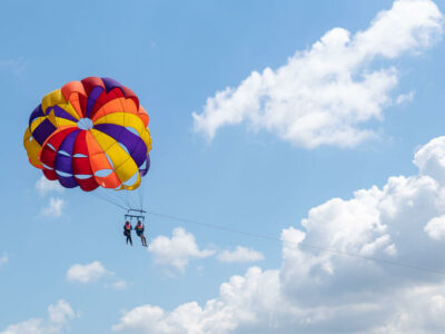 Dua orang berparasailing dengan parasut warna-warni di atas langit Bali yang cerah