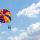 Dua orang berparasailing dengan parasut warna-warni di atas langit Bali yang cerah