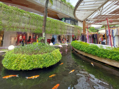 Pemandangan pusat belanja terbuka di Kuta dengan kolam ikan koi dan tanaman hijau